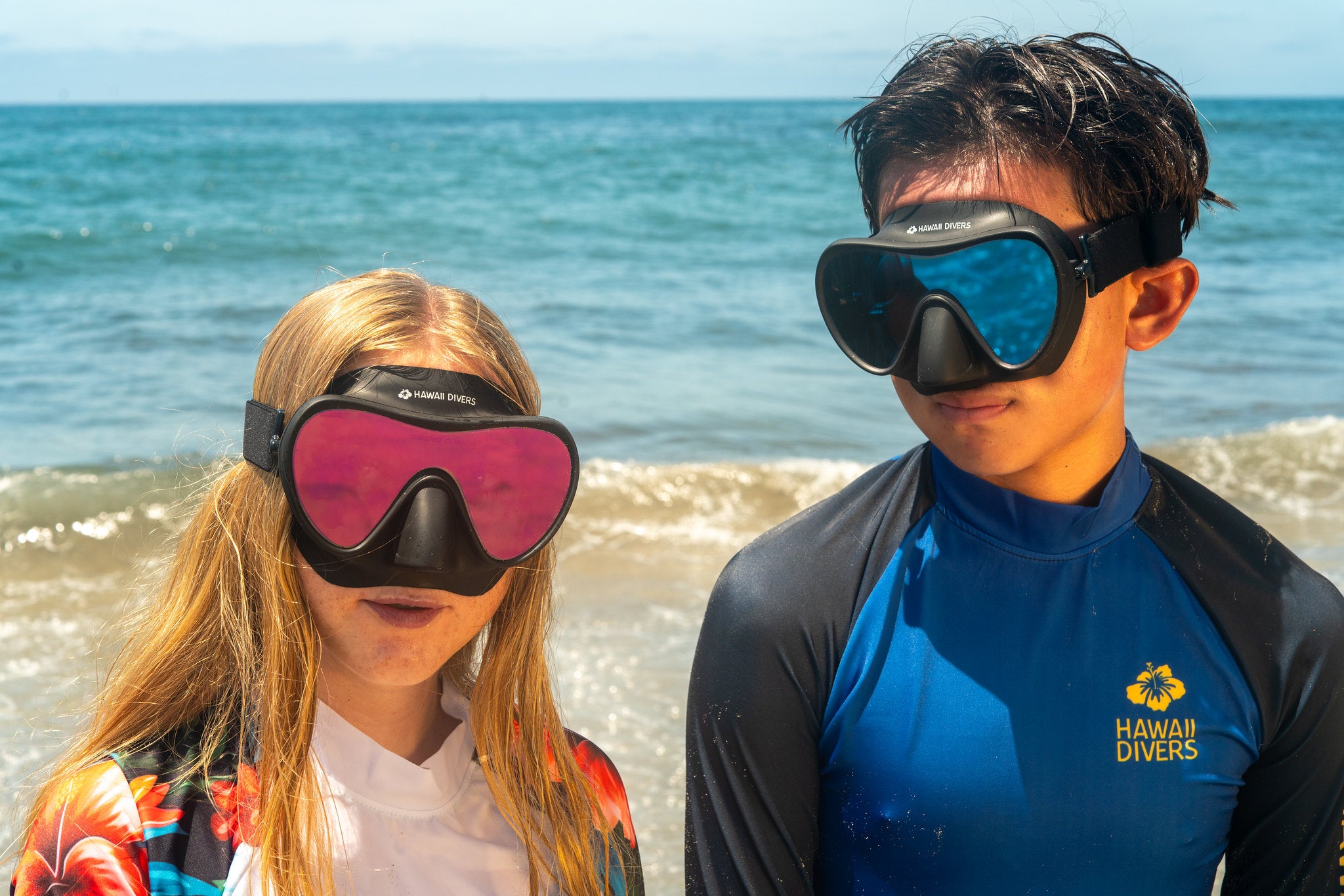 Two children wearing scuba diving masks on a beach with ocean in the background