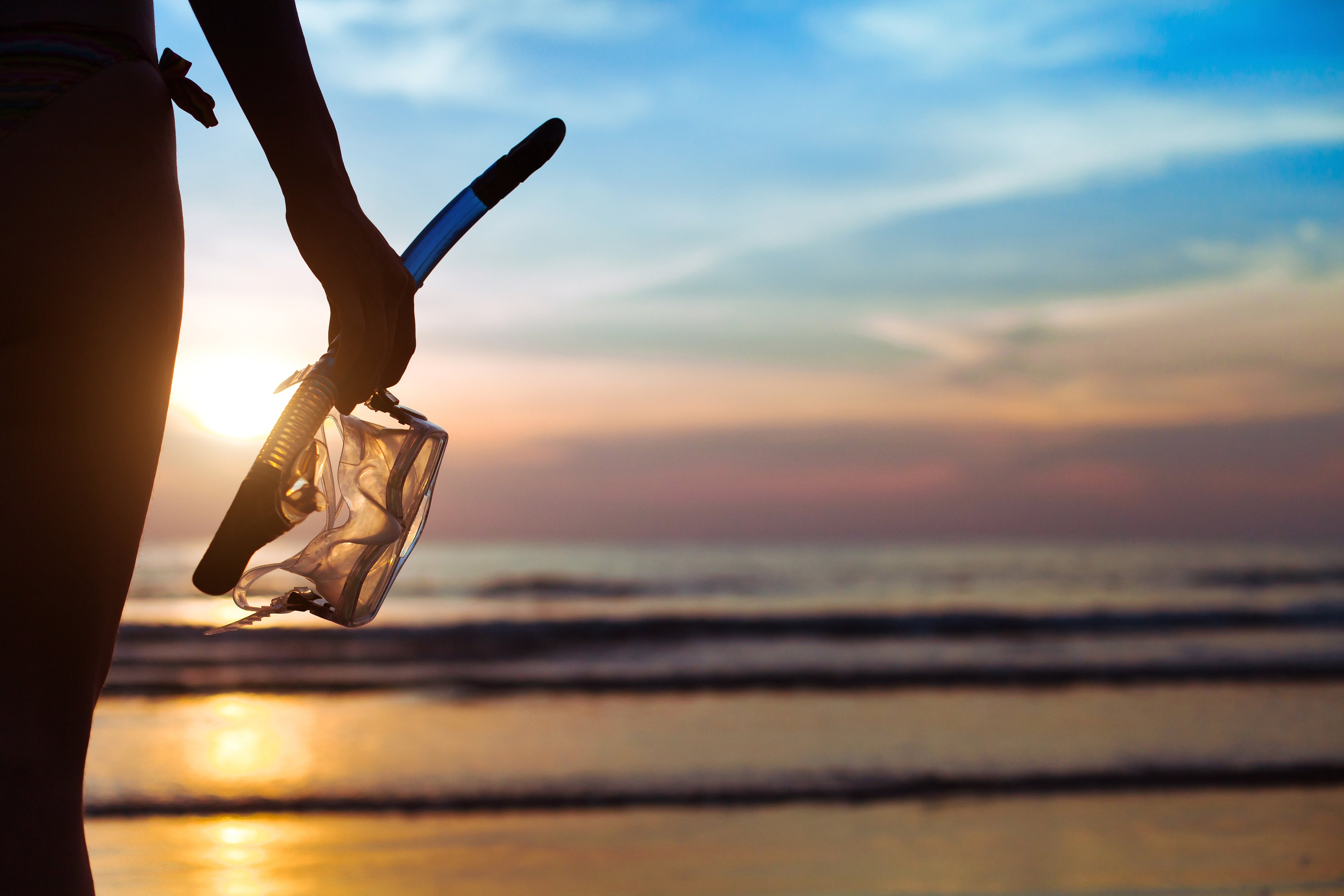 Person holding a snorkel mask on a beach at sunset