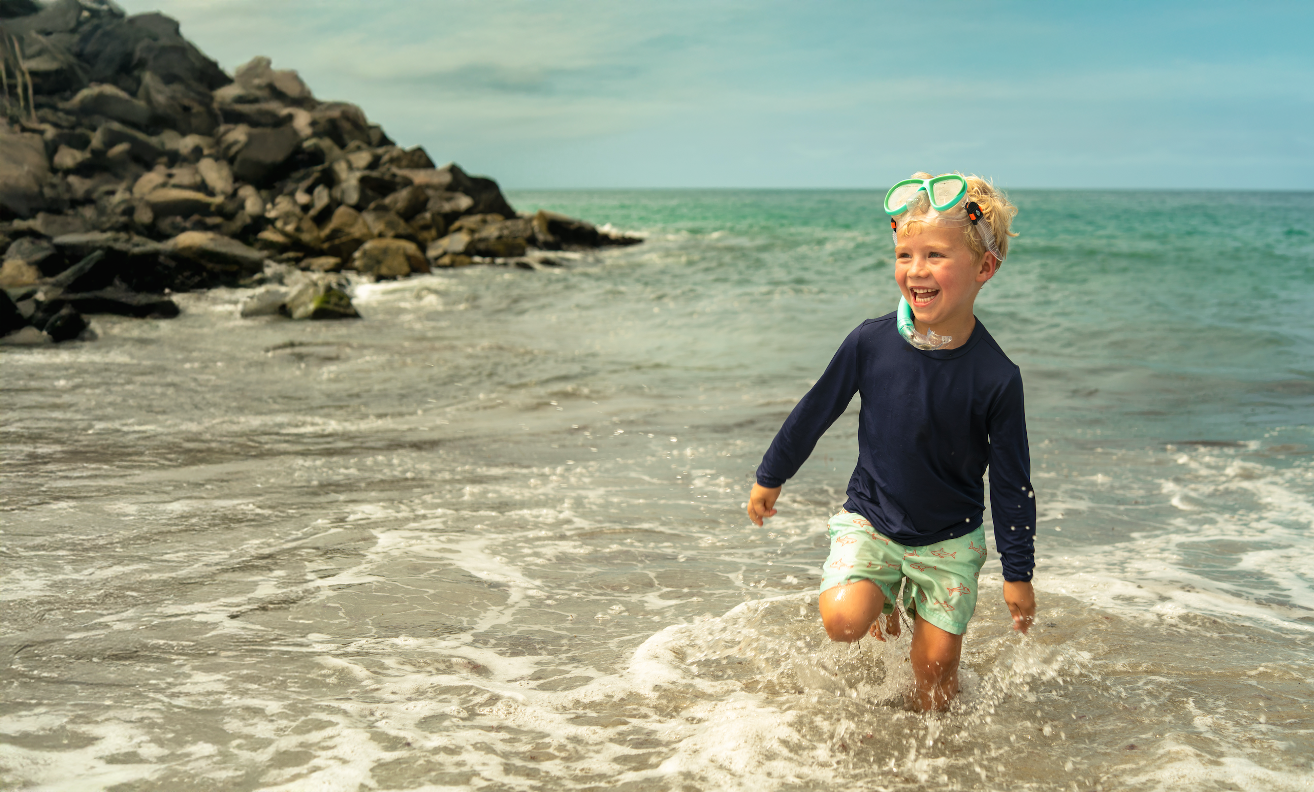 Child playing in the ocean with rocks and water in the background